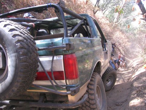 1989 Ford Bronco - A modified green SUV navigates a steep, dusty trail with people watching.