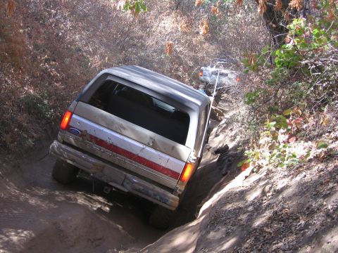 1989 Ford Bronco - A tan 1989 Ford Bronco navigates a steep, muddy off-road trail with another vehicle visible behind it.