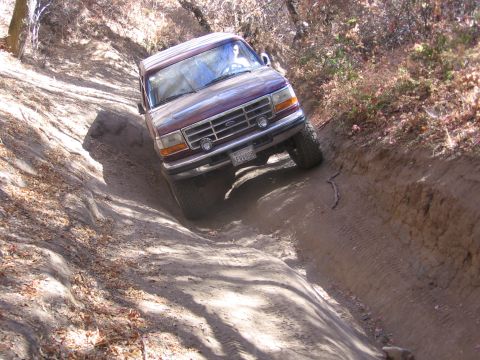 1989 Ford Bronco - Ford Bronco tackling a challenging off-road trail, kicking up dust on the descent.