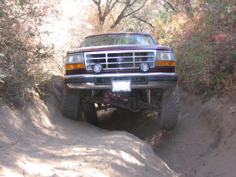 1989 Ford Bronco - A red Ford truck navigates a narrow dirt trail with steep banks.