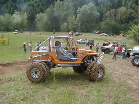 1988 Ford Bronco - An orange off-road buggy is the main subject in a field with several other vehicles and people present.