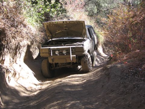 1989 Ford Bronco - This 1989 Ford Bronco navigates a challenging dirt path, its hood raised as if undergoing inspection or repair.