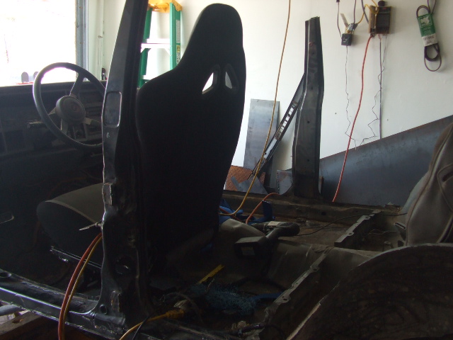 Black bucket seat on bare floor pan of stripped Jeep Cherokee interior during restoration in a garage