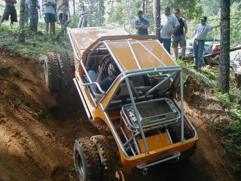 1988 Ford Bronco - An off-road vehicle navigates a steep, muddy incline with spectators watching from the treeline.