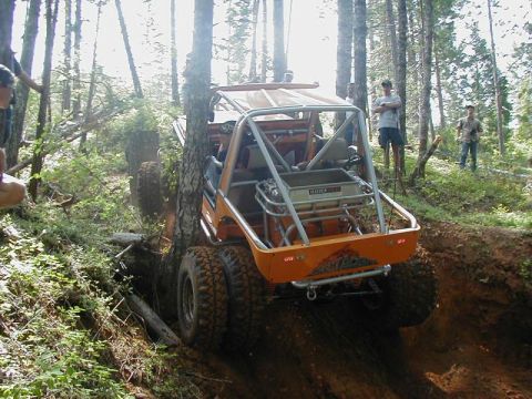 1988 Ford Bronco - An off-road buggy with a roll cage is seen from the rear as it maneuvers through a wooded area.