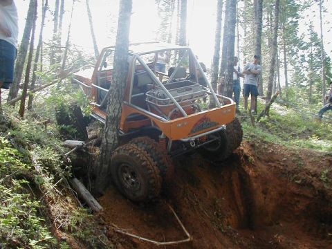 1988 Ford Bronco - An orange off-road vehicle navigates a challenging dirt incline in a wooded area.