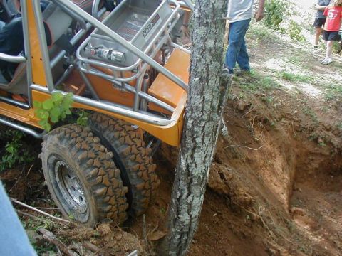 1988 Ford Bronco - An off-road buggy is stuck on a steep dirt embankment, with its tires deep in the mud next to a tree.