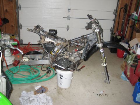 1993 Suzuki RMX250 - A motorcycle is partially disassembled in a garage, with parts and tools scattered around.