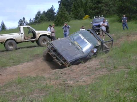 1988 Ford Bronco - Several people observe off-road vehicles navigating a steep, muddy incline on a wooded trail.