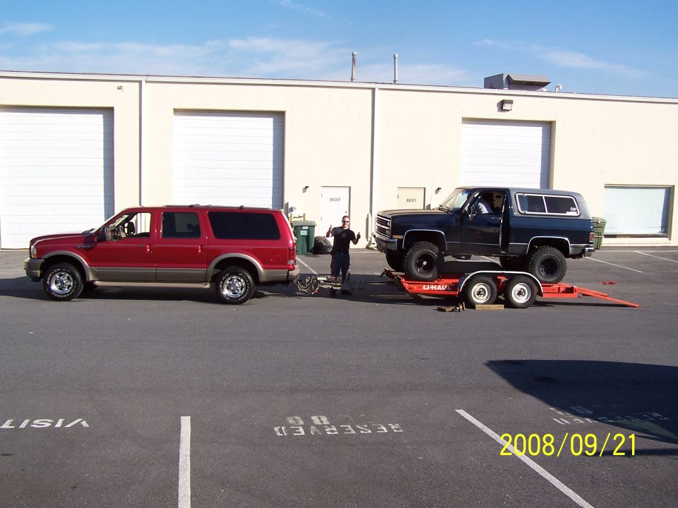 Maroon and tan Ford Excursion SUV in side view with a black Blazer on a U-Haul trailer behind it.