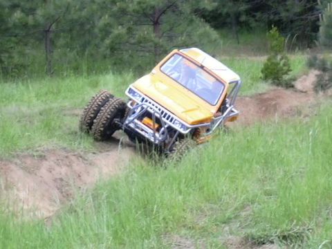 1988 Ford Bronco - A yellow off-road vehicle navigates a challenging grassy terrain with its dual rear tires.