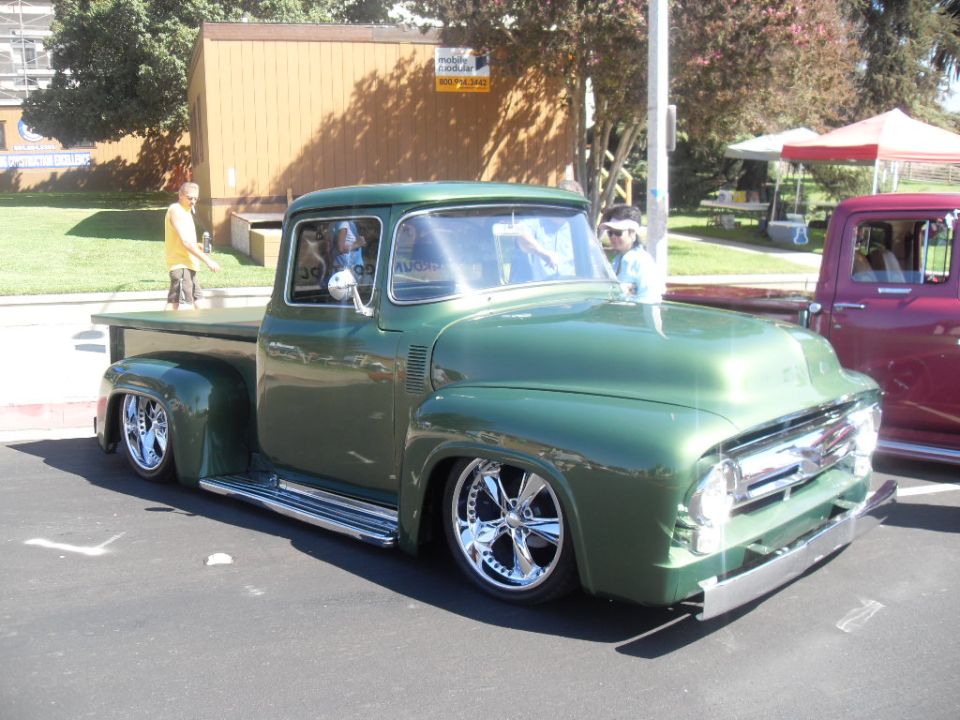 Green 1956 Ford F-100 pickup truck with custom wheels and lowered suspension. Another pickup is parked to the right