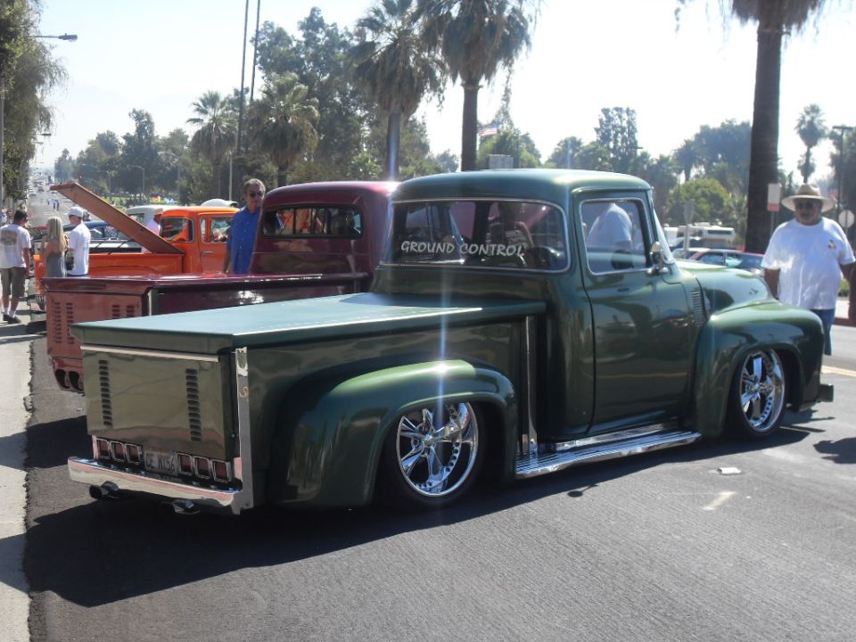 Green 1956 Ford F-100 pickup truck with custom wheels and lowered suspension, parked next to another truck