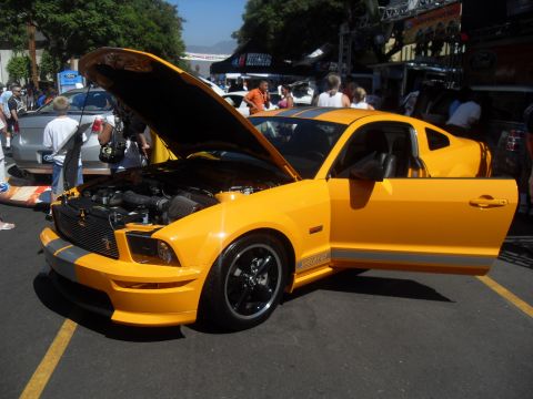 1990 Ford Bronco - Yellow Ford Mustang with hood and driver door open at an outdoor event.