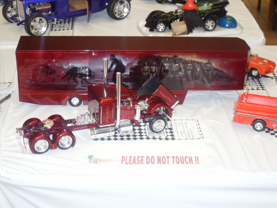 model semi-truck with hood open and custom painted trailer, other model cars in background