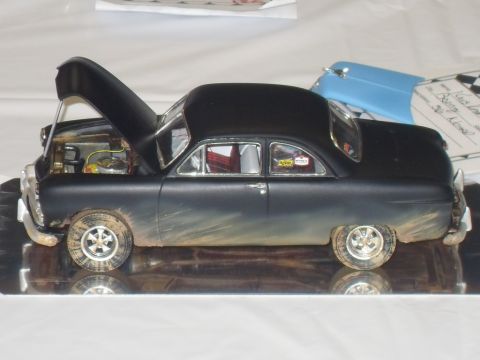1990 Ford Bronco - A black model car with its hood open sits on a reflective surface, with a blue car part in the background.