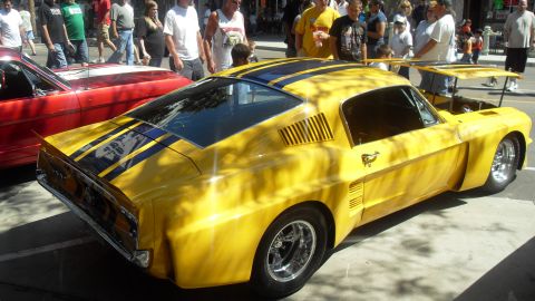 1990 Ford Bronco - A bright yellow custom coupe with racing stripes is displayed outdoors next to a red vehicle.