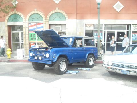 1990 Ford Bronco - A blue first-generation Ford Bronco is parked on a street with its hood open, next to another vehicle.
