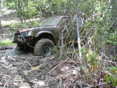 1988 Ford Bronco - This off-road vehicle is deeply stuck in mud and vegetation, suggesting a challenging trail.