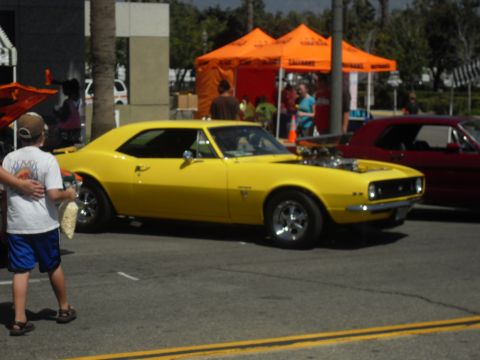 1990 Ford Bronco - A bright yellow classic muscle car with its hood open is displayed at an outdoor event.