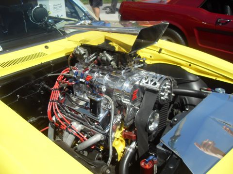 1990 Ford Bronco - A highly modified V8 engine with a prominent chrome supercharger is visible in the engine bay of a yellow car.