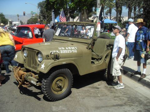 1990 Ford Bronco - A vintage US Army Jeep is displayed at an outdoor event, with onlookers gathered around.