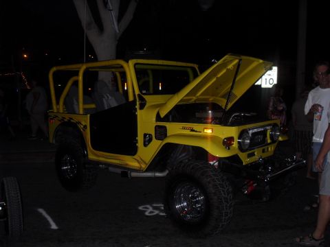 1990 Ford Bronco - A yellow off-road vehicle with its hood open is parked at night, with people standing nearby.