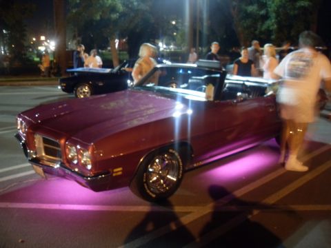 1990 Ford Bronco - A maroon convertible with purple underglow is parked at night, with other vehicles and people in the background.