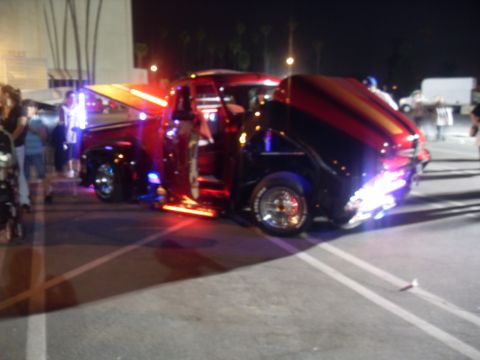 1990 Ford Bronco - A heavily modified pickup truck is displayed at night with its hood and doors open, illuminated by custom lights.