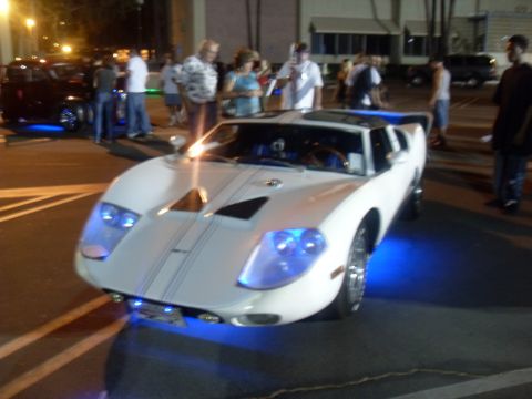 1990 Ford Bronco - A white sports car with blue underglow and racing stripes is parked at an event.
