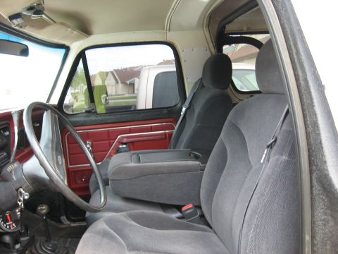 1979 Ford Bronco - The interior of the truck shows red door panels and grey seats, with another vehicle visible outside.