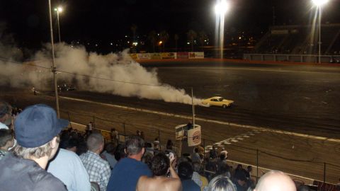 1990 Ford Bronco - A car creates a large cloud of smoke during a nighttime event, with a crowd observing from the stands.