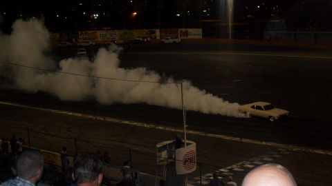 1990 Ford Bronco - A car performs a burnout on a track at night, creating a large cloud of smoke.