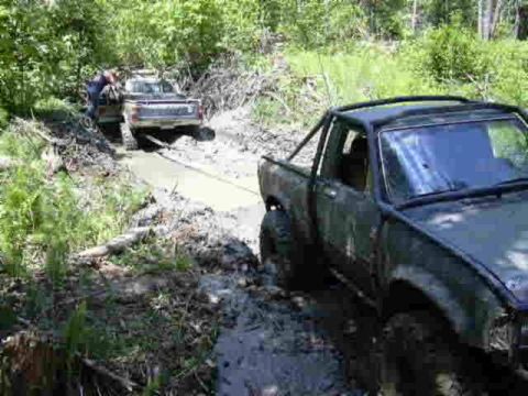 1988 Ford Bronco - Two trucks are stuck in a muddy off-road trail, with one vehicle being winched out by the other.