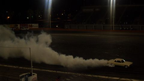 1990 Ford Bronco - A yellow car creates a thick smoke trail while performing a burnout on a dark track.