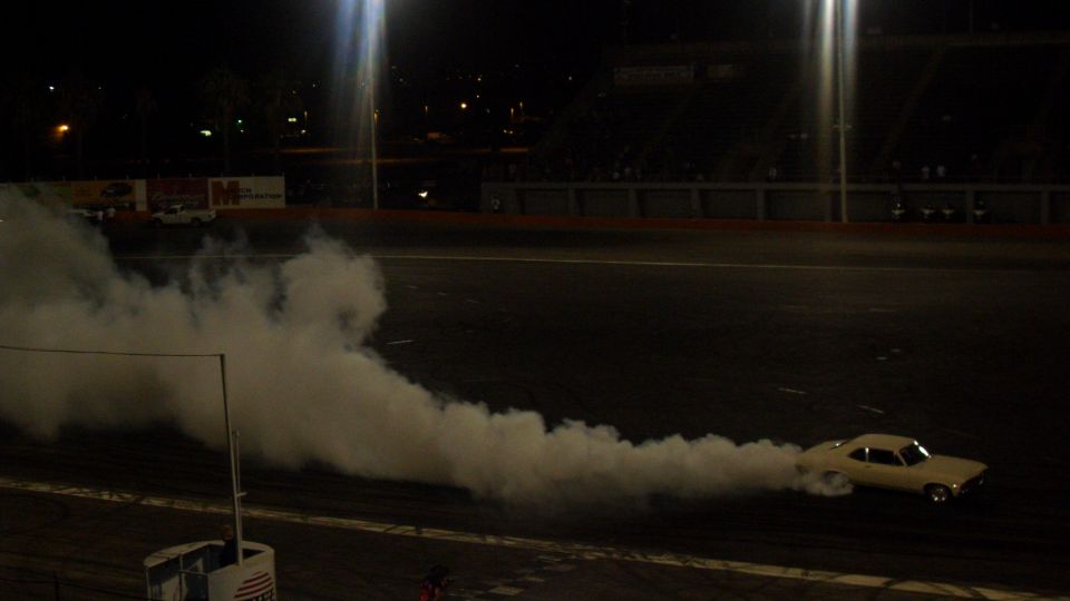 Yellow car performing a burnout on a track at night, emitting a large cloud of smoke