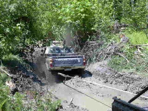 1988 Ford Bronco - Off-roading adventure: a truck struggles through a muddy trail with trees on either side.