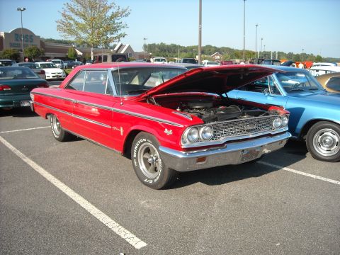 1979 Ford F-150 - A red 1964 Ford Galaxie 500 is displayed with its hood open at a car show, parked beside a blue vehicle.