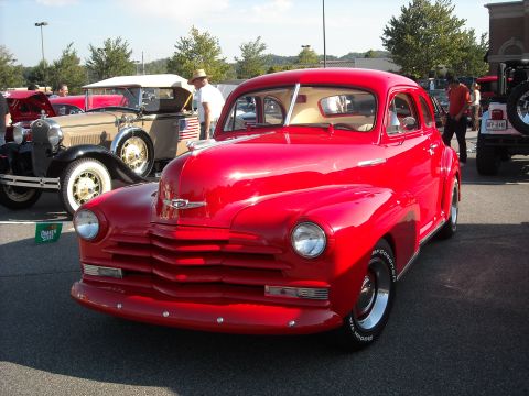 1979 Ford F-150 - A bright red vintage sedan is parked at a car show, with other vehicles visible in the background.