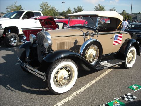 1979 Ford F-150 - A vintage convertible is parked in a lot with other vehicles, displaying an American flag on its fender.