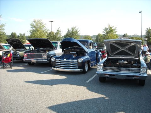 1979 Ford F-150 - A car show features multiple vehicles with their hoods open, including a blue pickup truck.