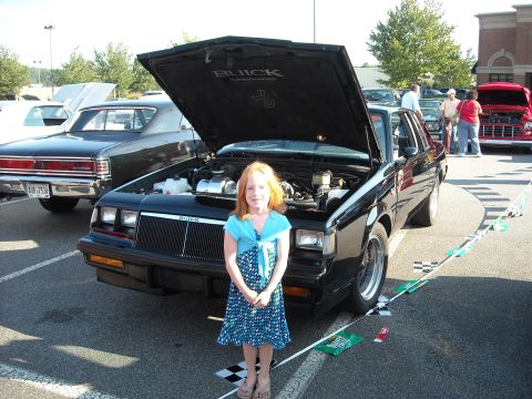 1979 Ford F-150 - A young girl poses in front of a black 1987 Buick Regal at a car show.