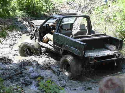 1988 Ford Bronco - A dark green off-road vehicle is stuck in mud with its front wheel submerged.