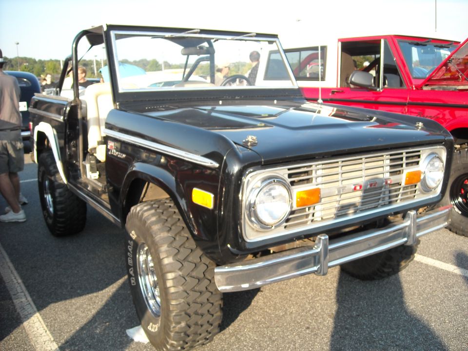 Black early Ford Bronco with folded windshield at a car show