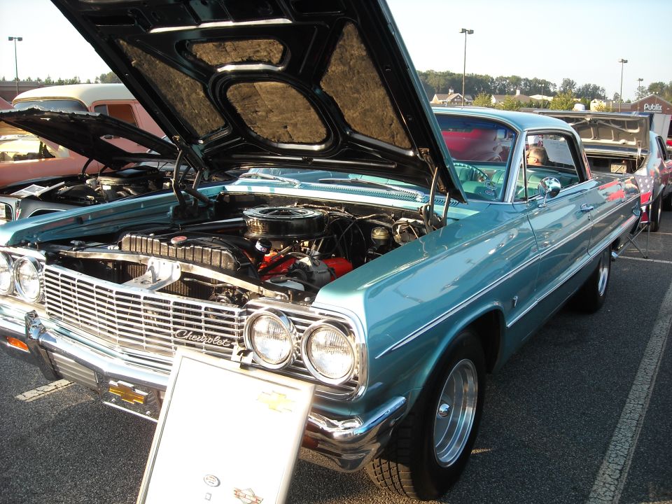 Teal 1964 Chevrolet Impala with hood open, showing engine. Another car is parked next to it