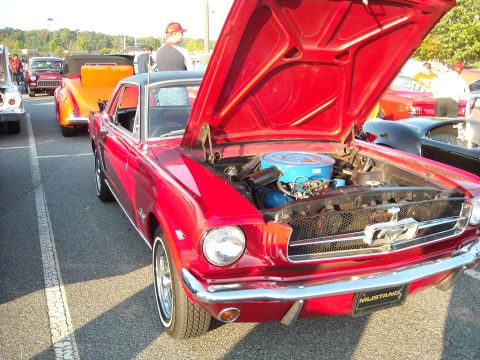 1979 Ford F-150 - A red 1965 Ford Mustang is parked at a car show, its hood raised to reveal the engine.