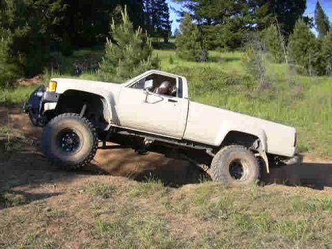 1988 Ford Bronco - A white pickup truck navigates an off-road terrain with large tires.