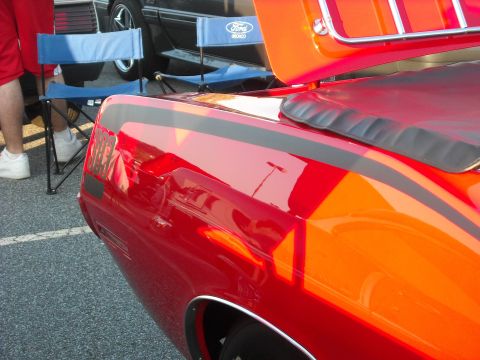 1979 Ford F-150 - A red and orange 1979 Ford F-150 is viewed from the rear quarter panel, with black racing stripes.