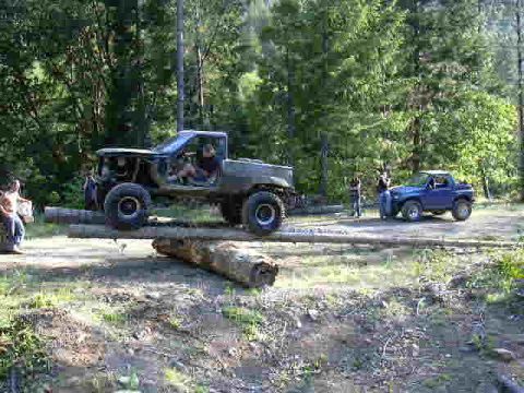 1988 Ford Bronco - Two off-road vehicles navigate a challenging course with large logs.