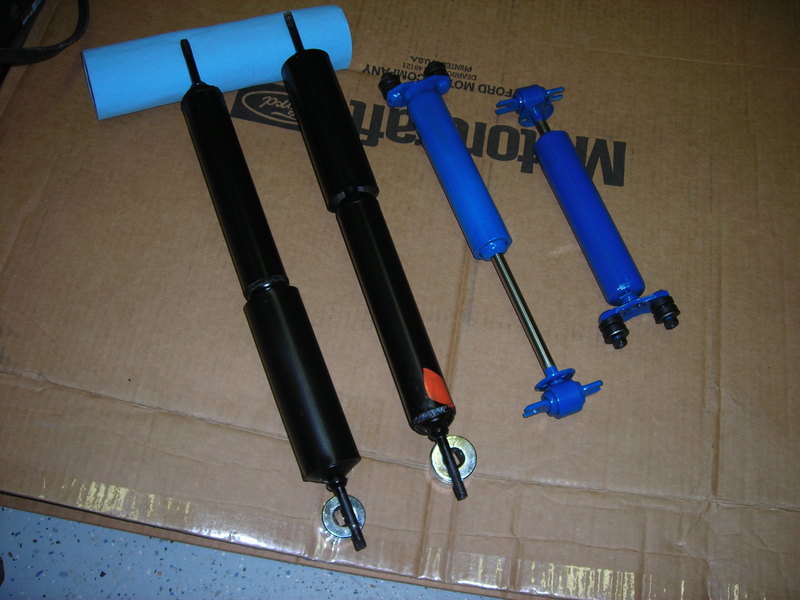 Four shock absorbers, two black and two blue, laid out on a surface